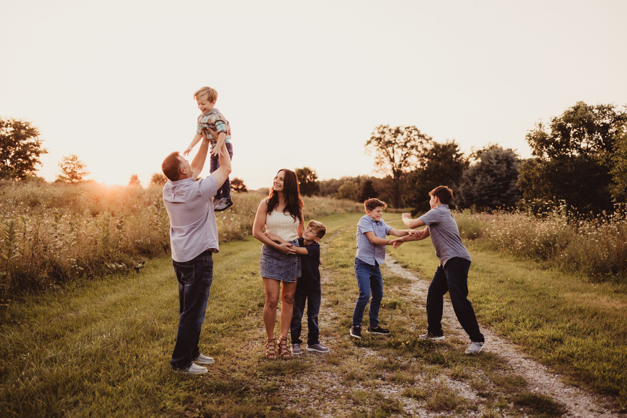 beautiful family with a husband wife and four boys having fun during the golden hour sunset